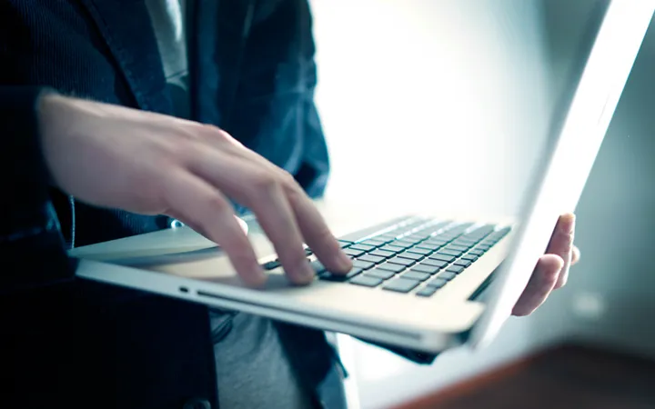 Person som håller i en laptop. Håller fingrarna på tangentbordet.